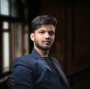 Young man in a dark suit jacket looking forward.